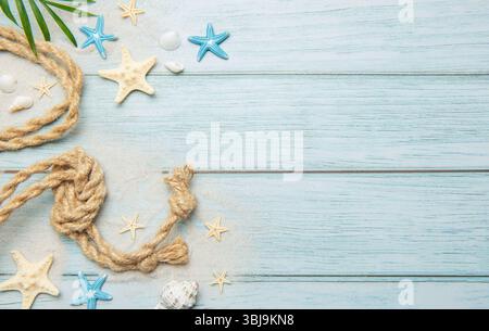 Summer marine decoration with palm leaf, seashells, starfishes and nautical rope lying on light blue wooden planks Stock Photo