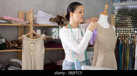 Young sewing woman professional measuring new dress at mannequin at atelier Stock Photo