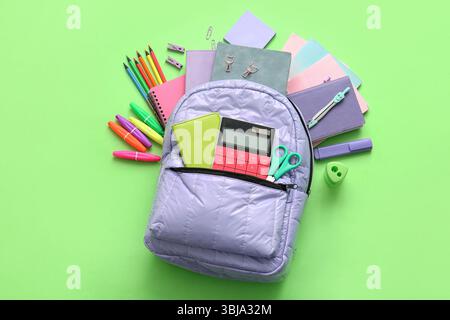 Lilac school backpack with different stationery supplies on green background Stock Photo