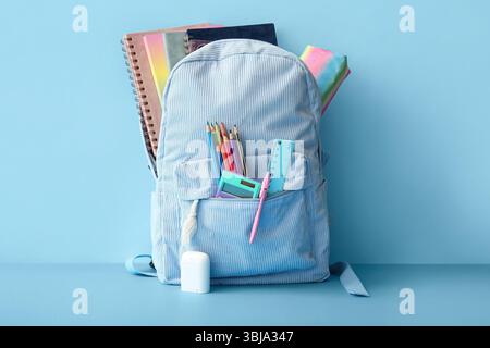 School backpack with different stationery on blue background Stock Photo