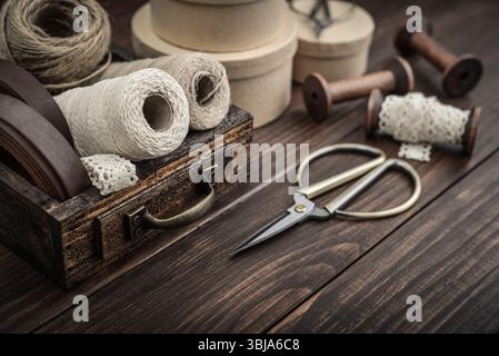 Tools and accessories for handicrafts or gift wrapping: bonsai scissors, jute rope, leather ribbon and spools  in vintage wooden box on dark wooden ba Stock Photo