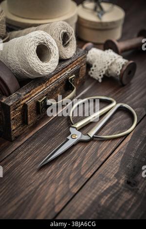 Tools and accessories for handicrafts or gift wrapping: bonsai scissors, jute rope, leather ribbon and spools  in vintage wooden box on dark wooden ba Stock Photo