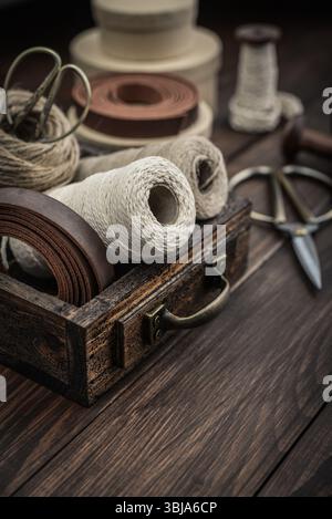 Tools and accessories for handicrafts or gift wrapping: bonsai scissors, jute rope, leather ribbon and spools  in vintage wooden box on dark wooden ba Stock Photo