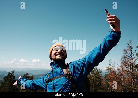 Happy tourist stretching arms wide for a selfie, enjoying the scenic view from Tornik peak. Serbia country during spring. Travel blogger making video Stock Photo