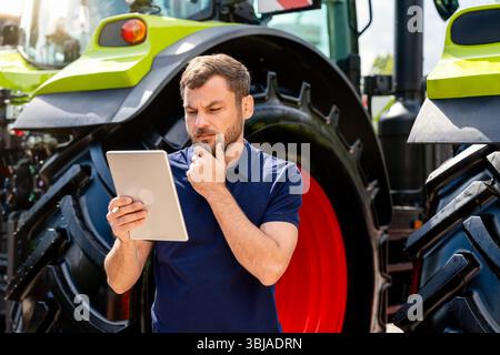 Thoughtful man analyzing information on digital tablet near tractor Stock Photo