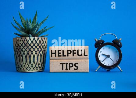 Helpful tips symbol. Wooden blocks with words Helpful tips. Beautiful blue background with alarm clock and succulent plant. Business and Helpful tips Stock Photo