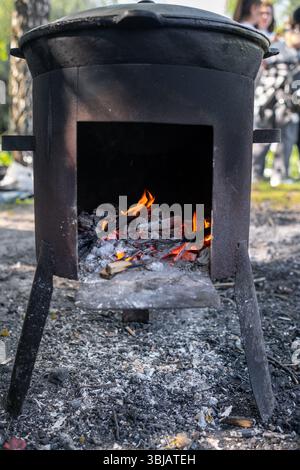 Fire Burns Brightly in a Rustic Metal Stove While Wood is Added for Cooking Outdoors in a Natural Setting During Daytime Stock Photo