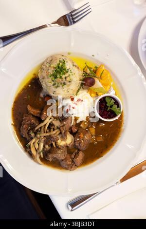 Delicious plate of austrian food with meat stew, herbs, vegetables, dumplings, and cranberry sauce, served in an elegant restaurant Stock Photo
