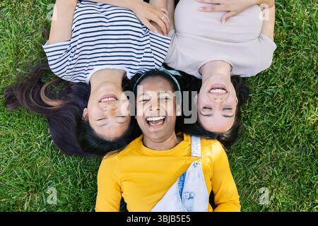 Three young women lying on grass smiling and enjoying summer day Stock Photo