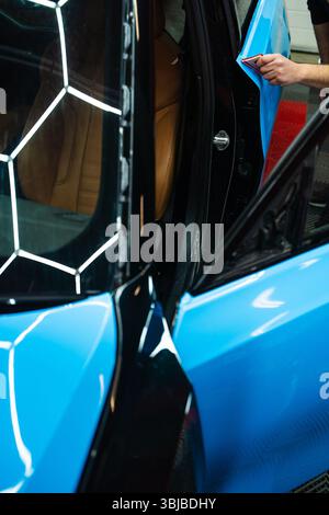 Car Flatten Pattern Detailing expert uses red squeegee wrapper to flatten blue PPF wrap on ...