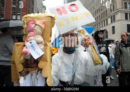 An anti-Trump demonstrator marches holding a placard and a doll of Donald Trump. Demonstrators in Manhattan protested against Donald Trump on his birthday in a “No Kings” rally. Protesters claimed Trump is acting as if he has ultimate power and challenging the government's checks and balances system. Demonstrators condemned Trump's immigration policies and the U.S. Immigration and Customs Enforcement or ICE for arresting and deporting immigrants. The protest comes amid protests in Los Angeles and in cities nationwide opposing ICE immigration raids. Stock Photo