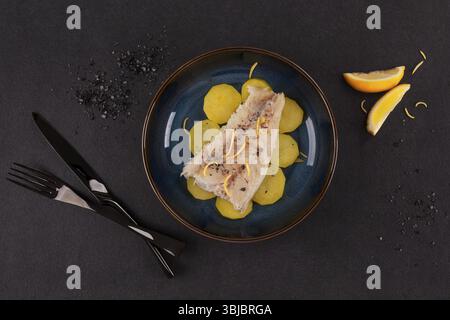 Grilled fish fillet served with potatoes on plate over black background. Culinary eating Stock Photo