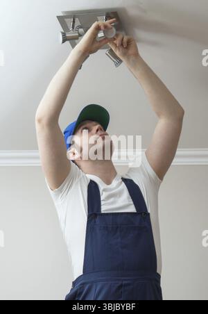 Electrician changing fluorescent light bulb in ceiling light fixture ...