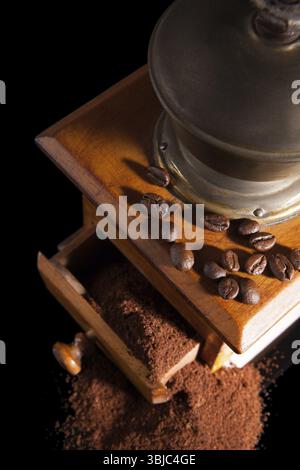 Old vintage coffee mill with ground coffee isolated on black background, top view. Elegant coffee still life Stock Photo