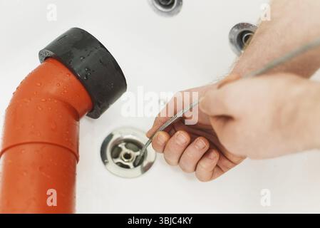 Plumber using drain snake to unclog bathtub Stock Photo