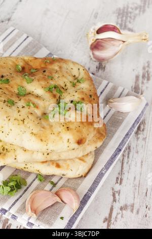 Luxurious naan flatbread background. Naan stack with fresh cilantro and garlic on white wooden textured background. Culinary traditional asian bread e Stock Photo