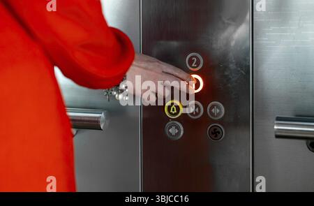 Woman in red dress pressing button inside elevator Stock Photo