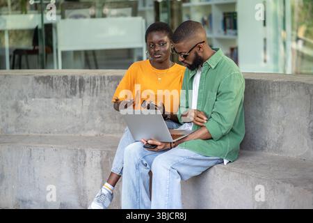 Focused African American multiracial couple work on laptop outdoors, prepare for exams, remote study Stock Photo