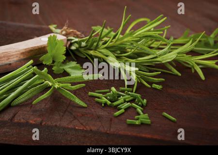Fresh herb mixture on dark wooden cutting board. Chive, rosemary, coriander and arugula, aromatic culinary herbs Stock Photo