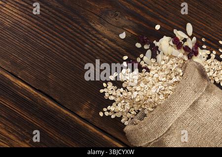 Oatmeal flakes, Cranberries and almonds in burlap bag on brown wooden table from above Stock Photo