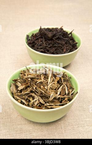 Green and black tea leaves in green bowls on brown natural background Stock Photo