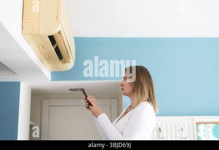 Woman controls a smart air conditioner using a remote control on her phone Stock Photo