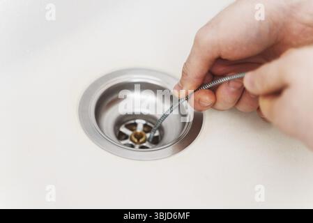 Plumber using drain snake to unclog kitchen sink Stock Photo