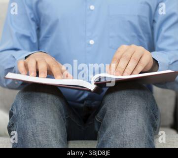 Blind man reading braille book on the couch Stock Photo