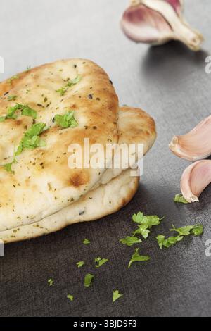 Naan flatbread stack with fresh cilantro herb and garlic on dark black and grey background. Culinary eastern background Stock Photo