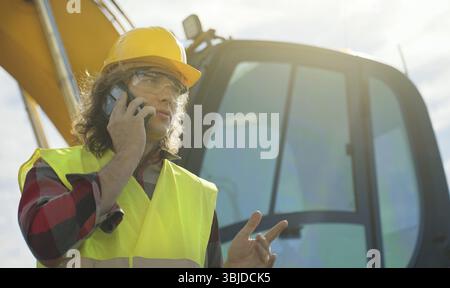 Excavator operator in hard hat talking by smartphone Stock Photo
