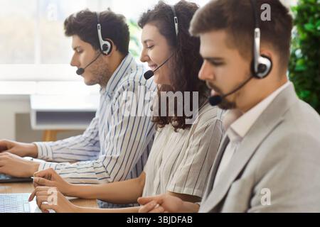 Call center operators in headsets sitting at desk and helping clients with support requests. Stock Photo
