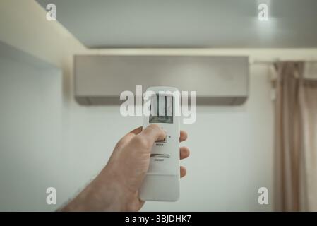 Hand holding remote control in front of the air conditioner Stock Photo