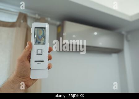 Hand holding remote control in front of the air conditioner Stock Photo