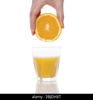 Freshly squeezed orange juice. Female hand squeezing orange into a glass isolated on white background. Healthy juice drink Stock Photo