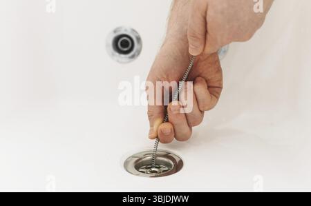 Plumber using drain snake to unclog bathtub Stock Photo