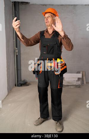 retired builder making videocall or selfie on smartphone over room background. construction, profession and repair Stock Photo