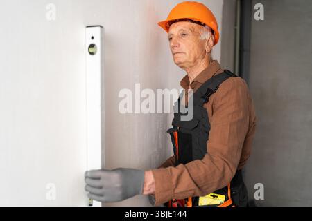 Builder elderly man using a spirit level measuring wall in new house Stock Photo