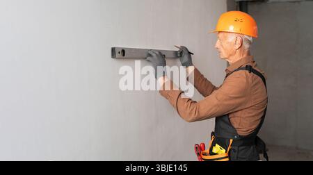 Elderly male builder using spirit level checking the leveling of a wall. Profession, construction and building Stock Photo