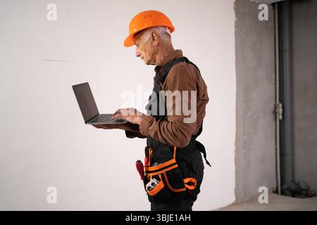 professional male builder showing construction on new house. civil engineer in safety helmet using laptop computer Stock Photo