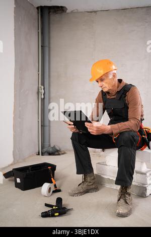 Civil engineer elderly man with clipboard reading checklist making inspection notes working at construction site. Repair, renovation and construction Stock Photo