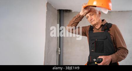 Sad elderly construction worker taking off helmet suffering from depression and job problems at building site Stock Photo