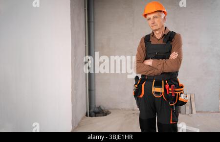 Elderly mature male builder in safety helmet serious with crossed arms. profession, construction and building Stock Photo