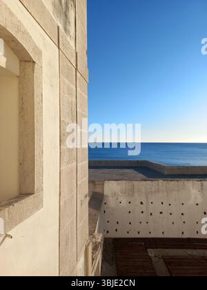 Sunlight glinting on Atlantic waves as they gently reach Sesimbra’s golden sandy beach, captured from a coastal viewpoint. Stock Photo