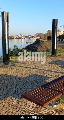 Quiet dawn scene at Seixal promenade featuring empty bench cobbled path riverside tree and serene reflection of opposite buildings across the water Stock Photo