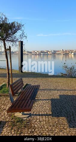 Quiet dawn scene at Seixal promenade featuring empty bench cobbled path riverside tree and serene reflection of opposite buildings across the water Stock Photo