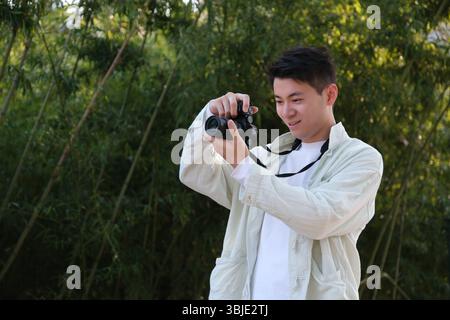 handsome Asian young man taking photo using digital camera outdoor Stock Photo
