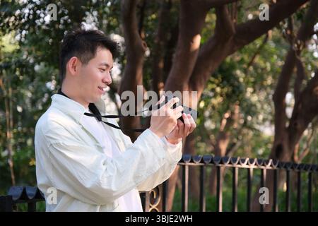 Chinese young man take photos use camera outdoor, side view Stock Photo