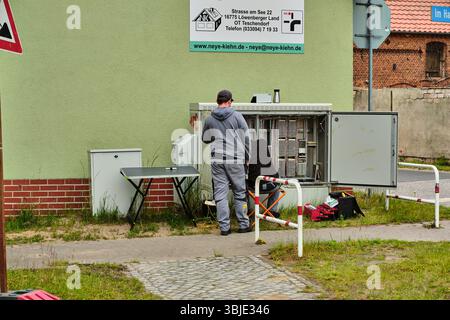 June 10, 2025 – Teschendorf, Germany: Two technicians connect and splice fiber optic cables inside an open telecom cabinet during a rural infrastructu Stock Photo