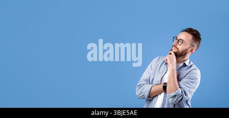 Pensive Caucasian guy thinking over decision or problem, looking at empty space over blue studio background Stock Photo