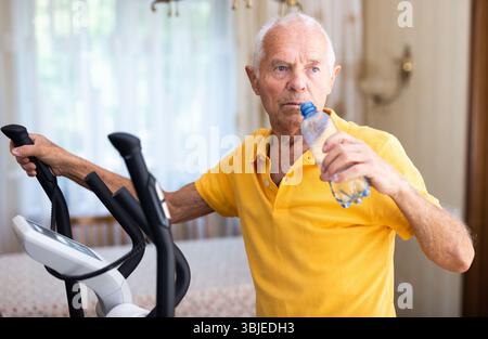 Senior man using elliptical trainer and drinking water Stock Photo
